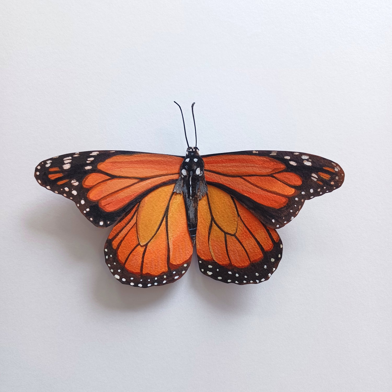 An orange monarch butterfly sculpture sits on a white table.