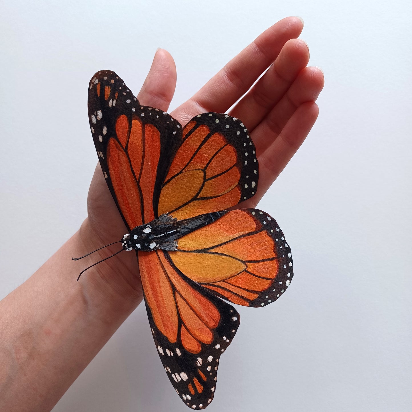 An orange monarch butterfly sculpture sits on a hand to show scale..