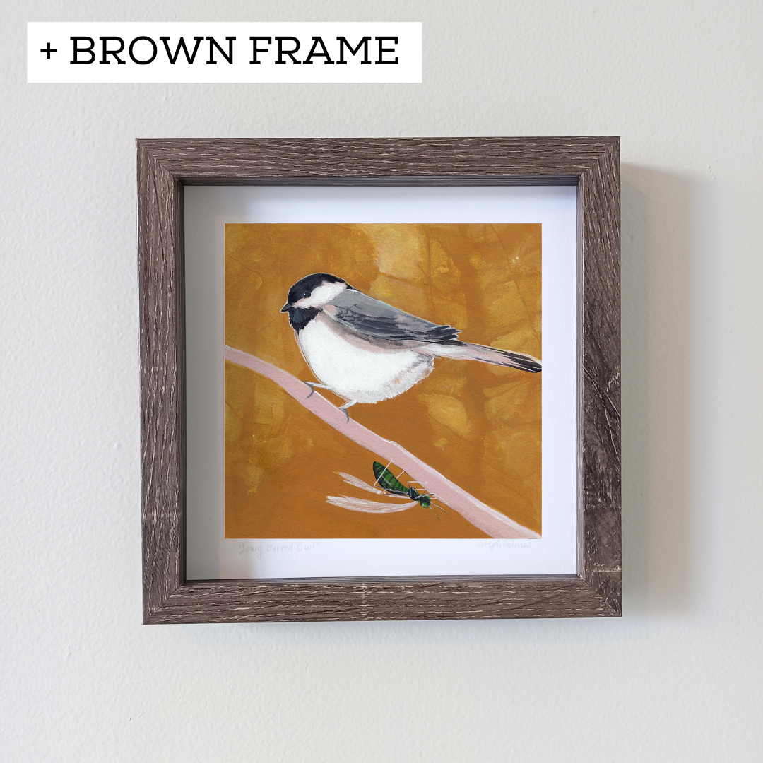 An art print featuring a black capped chickadee bird with a yellow background in a brown frame on a white wall.